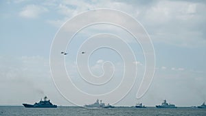 Helicopter silhouettes fly over naval vessels at parade