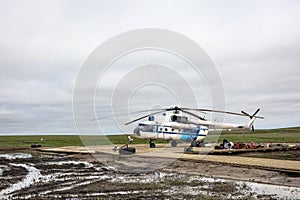 A helicopter sits on a wooden heliport in the tundra.