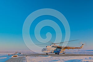 A helicopter sits on a wooden heliport in the tundra.