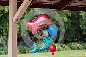 Helium filled birthday party balloon in a shape of a mermaid with two smaller blue and red balloons