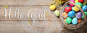 Hello April card. Colorful Easter eggs and mimosa flowers on wooden background, flat lay. Banner design