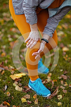 Hello autumn. Closeup on woman in fitness clothes in the park with knee pain