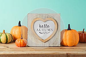 Hello Autumn concept with heart shape photo frame and pumpkin decor on wooden table over blue background