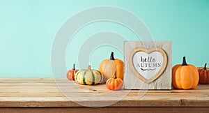 Hello Autumn concept with photo frame and pumpkin decor on wooden table over blue background. Fall season greeting card