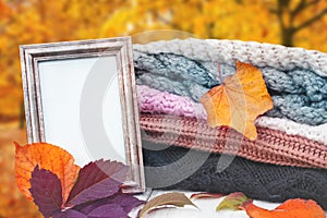 Hello autumn. A stack of knitted winter clothes, colorful autumn leaves and an old empty picture frame with copy space on a table