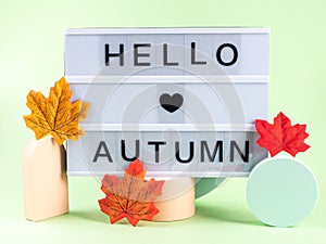 Hello autumn text on lightbox with fall leaves on green and orange podiums