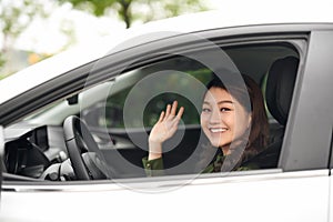 Hello! Beautiful young cheerful woman looking at camera with smile and waving while sitting in her car