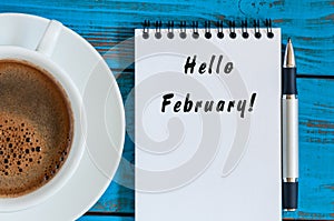 Hello february - inspiration in notepad near cup of morning coffee at workplace or ather blue table. Top view, winter