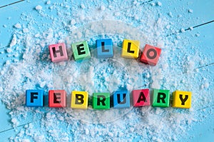 Hello February written on colour wooden toy cubes On light background with snow