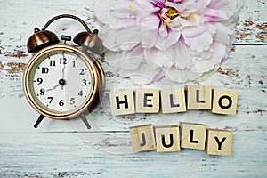 Hello July with alarm clock on wooden background