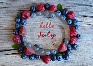 Hello July greeting card with text with with fresh ripe berries on old wooden background.Blueberry and raspberry.Summertime concep