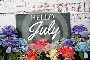 Hello July typography text decorate with flower on wooden background