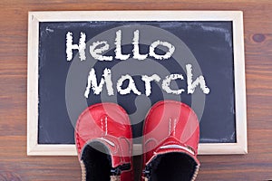 Hello March and kid shoes on on chalkboard and wooden backgroundr