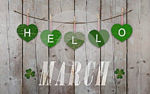 Hello March written on hanging green hearts and weathered wooden background