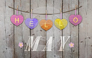 Hello May written on hanging pink and orange and purple hearts and weathered wooden background