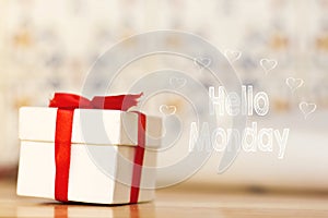Hello monday message with white gift box with red ribbon on wood background