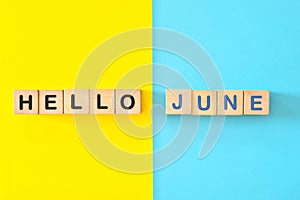 Hello month of June concept. Wooden blocks typography in bright blue and yellow background.