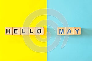 Hello month of May concept. Wooden blocks typography in bright blue and yellow background.