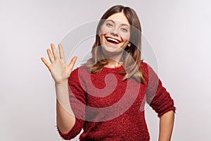 Hello, nice to meet you! Portrait of happy brunette girl in shaggy sweater raising hand waving hi and smiling friendly