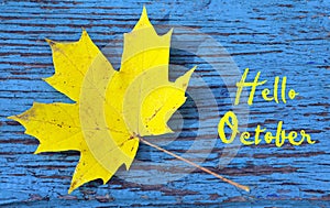 Hello October.Golden autumn maple leaf on a blue colored vintage wooden texture.Autumnal background with text.