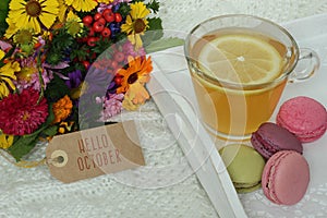 Hello October text on label, autumn flowers and cup of tea