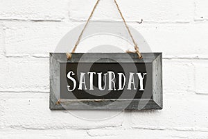 Hello saturday text on hanging board white brick outdoor wall photo