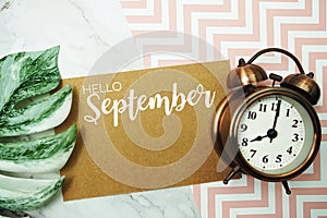 Hello September typography text on paper card with alarm clock and Monstera leave