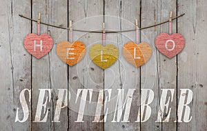 Hello September written on hanging yellow, red and orange hearts, on wooden planks background