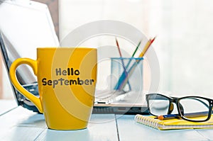 Hello September written on yellow coffee cup at teacher or student workplace. Back to school time