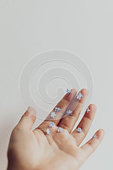 Hello spring. Simple aesthetic image. Cute little blue flowers on hand and fingers against white wall. Delicate forget me not