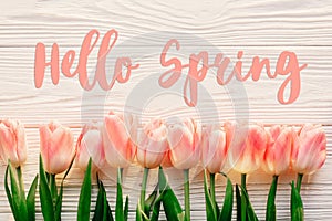 hello spring text sign, beautiful pink tulips on white rustic wooden background flat lay. flowers in soft morning sunlight with s