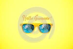 Hello Summer concept image: yellow sunglasses with palm tree reflections isolated in large yellow background.