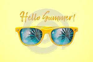 Hello Summer concept image: yellow sunglasses with palm tree reflections isolated in pastel yellow background.