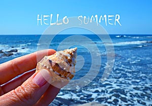 Hello Summer greeting card with hand holding sea shell on a blue ocean water background.