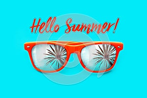 Hello Summer text Orange sunglasses with palm tree reflections isolated in intense cyan background. Minimal image concept.