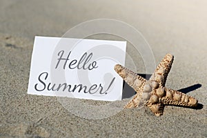 HELLO SUMMER text on paper greeting card on background of starfish seashell summer vacation decor. Sandy beach sun coast