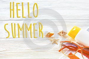 hello summer text, vacation concept. colorful towel, sunglasses, yellow sunscreen and star shells on white rustic wooden