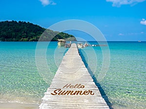 Hello Summer, text on wooden bridge heading to the boat pier on blue sea. Wood plank pathway bridge on the beach.