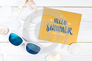 Hello Summer word on gold paper card white Summer Beach accessories (White sunglasses,starfish,straw hat,shell) on white plaster