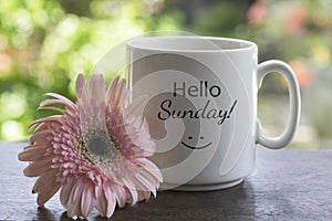 Hello Sunday. Relax Sunday concept with a cup of morning coffee or tea and a happy smiling sign on it and a flower on the table.