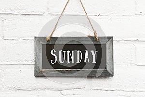 Hello sunday text on hanging board white brick outdoor wall