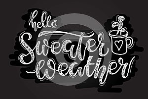 Hello Sweater Weather. Handwritten Lettering with cup of hot drink sketch on black chalk board. Autumn Winter
