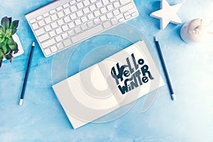 Hello winter graphic handlettering in Open notebook with keyboard on blue table top view flat lay mock up