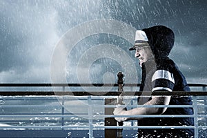 Helmsman with vest and cap struggle against storm in front of st photo