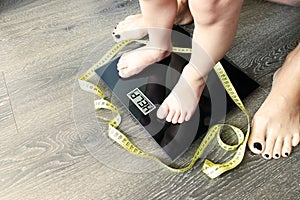 Help fat or obese child with toddler on weight scale, supervised by a parent