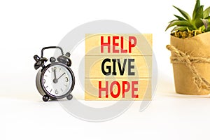 Help give hope symbol. Concept word Help give hope on beautiful wooden block. Black alarm clock. Beautiful white table white