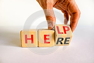 Help is here support symbol. Businessman turns the wooden cube and changes the concept word Help to Here. Beautiful white table