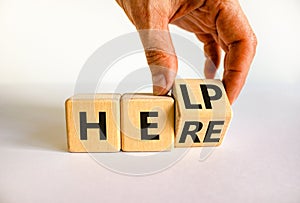 Help is here support symbol. Businessman turns the wooden cube and changes the concept word Help to Here. Beautiful white table