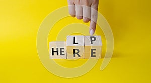 Help is here symbol. Businessman hand points at cube with words Here to Help. Beautiful yellow background. Business and Help is