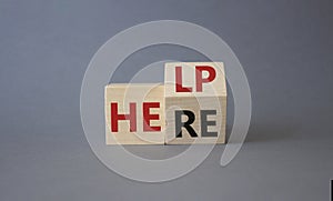 Help is here symbol. Turned wooden cube with words Here to Help. Beautiful grey background. Business and Help is here concept.